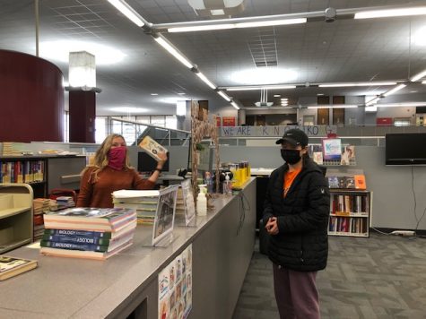 Principal Kelly Cooper helps freshman Angelina Chen check out a novel for her English class on Jan. 12. Students are in distant learning until at least March, but occasionally come to campus for materials and books.